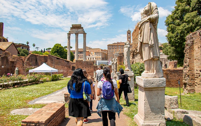 Visitors exploring the Roman Forum with ancient statues and ruins in Rome, Italy.