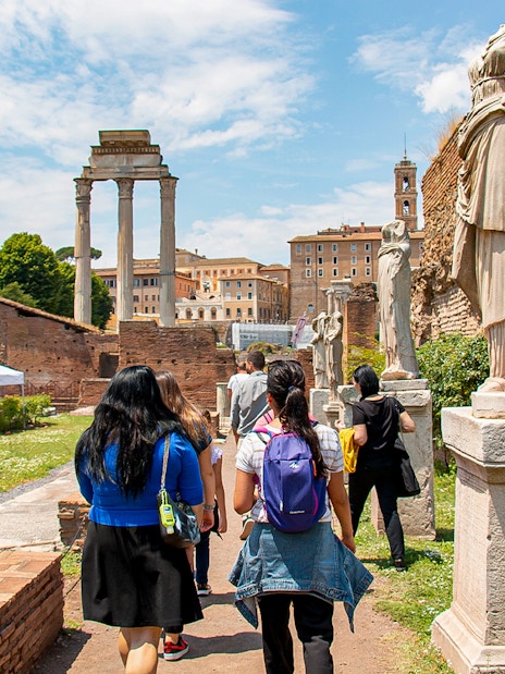Visitors exploring the Roman Forum with ancient statues and ruins in Rome, Italy.