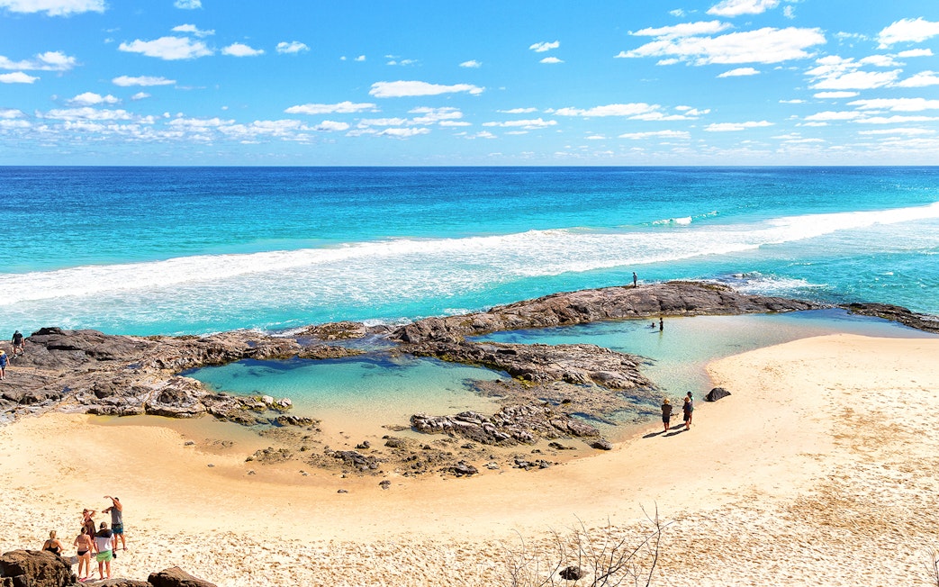 People exploring rock pools on K'gari (Fraser Island) beach during a guided tour.
