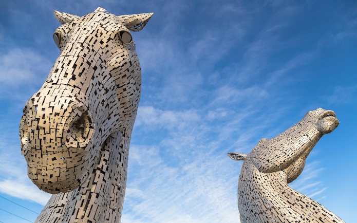 Kelpies horse-head sculptures at The Helix Park, Scotland against blue sky.