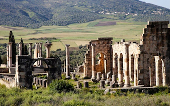 Ancient Roman ruins of Volubilis with green hills in the background, near Fes, Morocco.