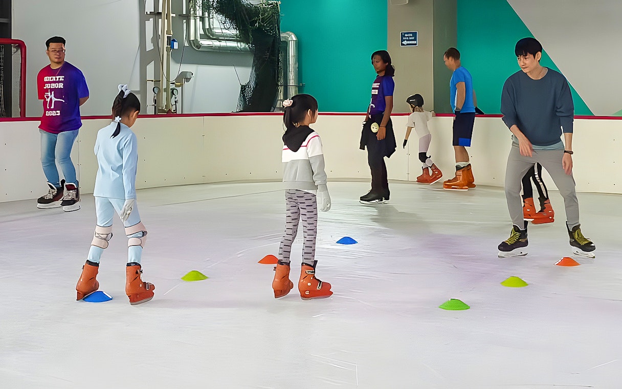 Ice skating lesson at Blue Ice Snow Park, children and adults practicing on rink.