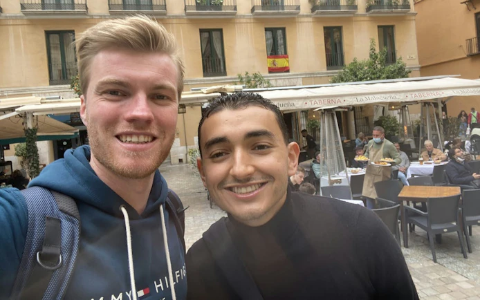 Selfie in a Malaga plaza with outdoor dining and Spanish flag in background.