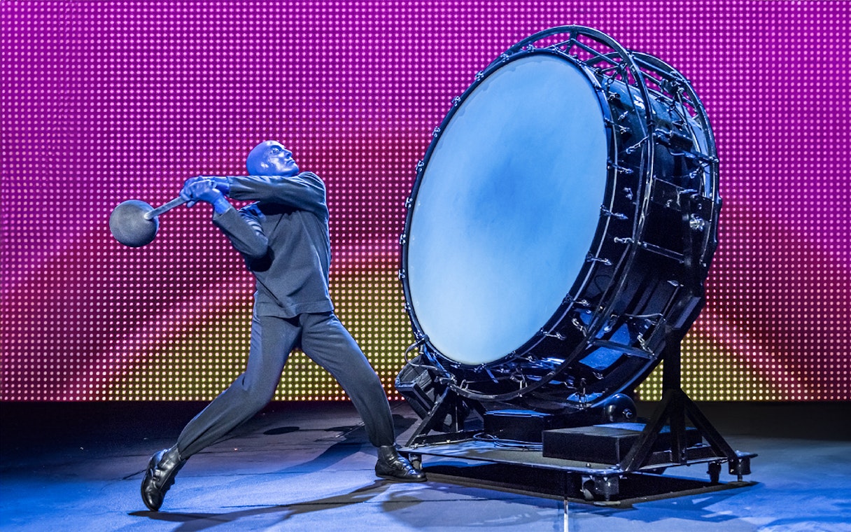 Performer from Blue Man Group playing a large drum on stage.