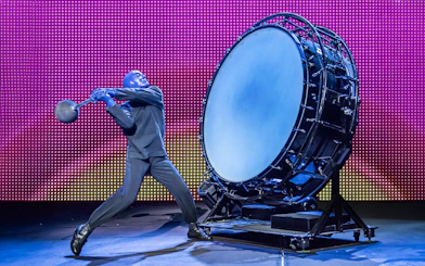 Performer from Blue Man Group playing a large drum on stage.
