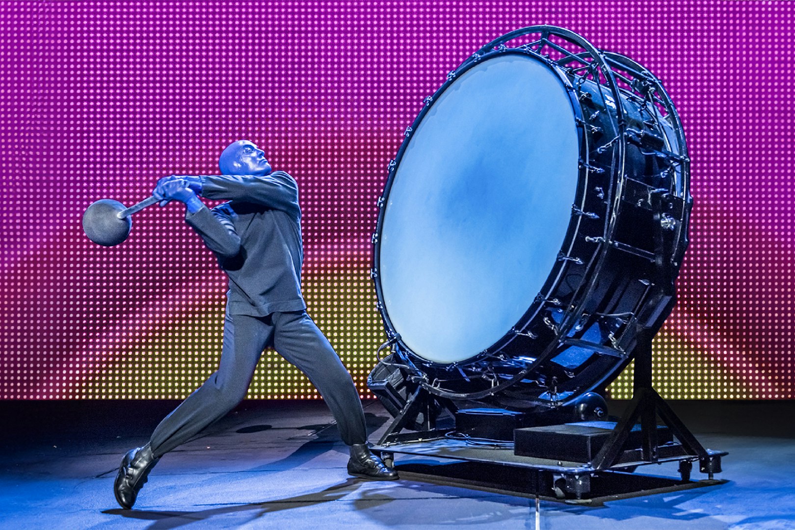 Performer from Blue Man Group playing a large drum on stage.