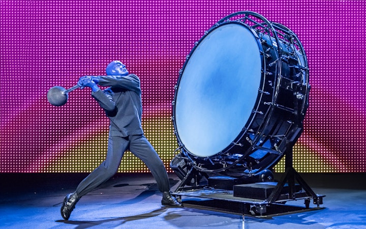 Performer from Blue Man Group playing a large drum on stage.