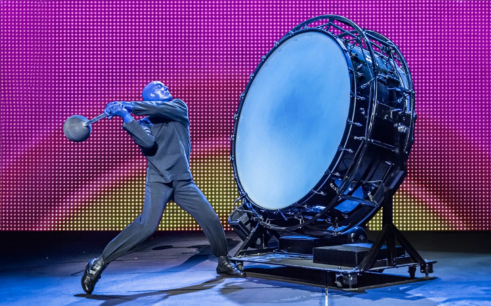 Performer in blue hitting a large drum during Blue Man Group show.