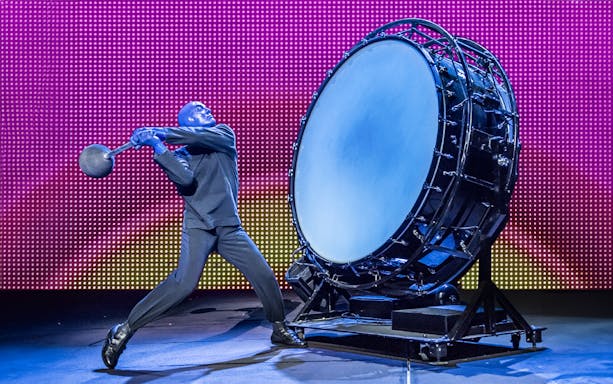 Performer in blue hitting a large drum during Blue Man Group show.