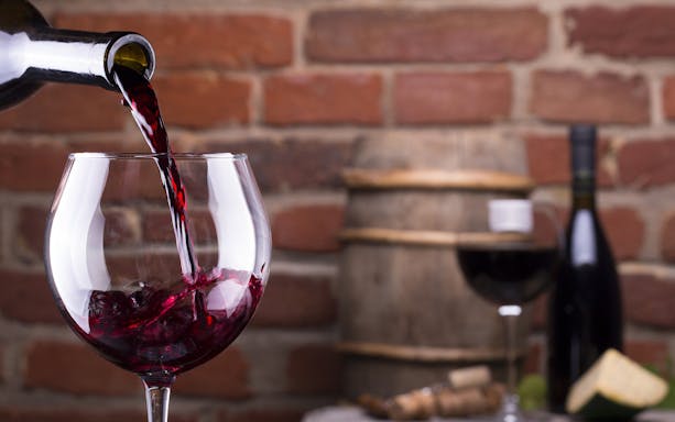 Pouring red wine into a glass with a wine barrel in the background, Erice & Marsala tour.