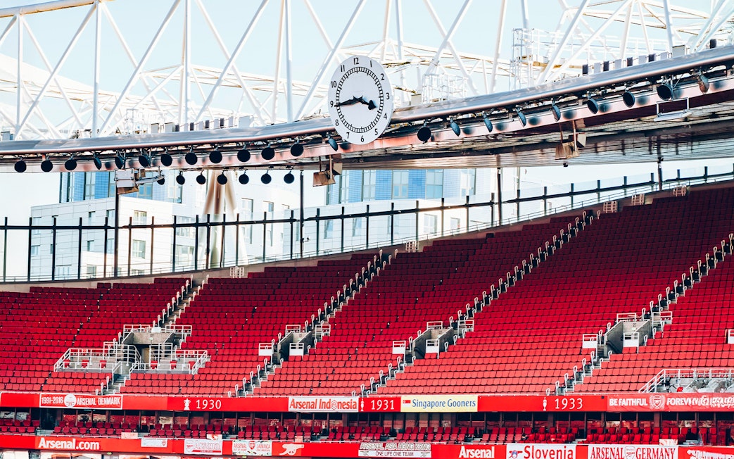 Red seating and iconic clock inside Emirates Stadium, London.