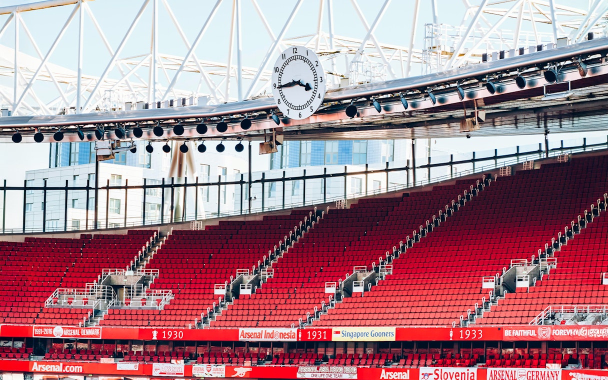 Red seating and iconic clock inside Emirates Stadium, London.