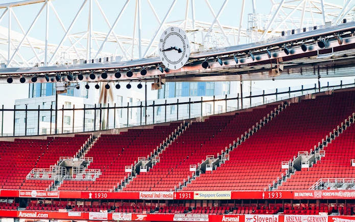 Red seating and iconic clock inside Emirates Stadium, London.