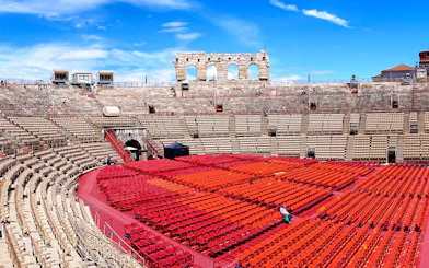 Verona Arena seating area with red chairs under a blue sky.