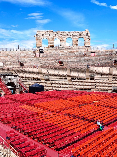 Verona Arena seating area with red chairs under a blue sky.