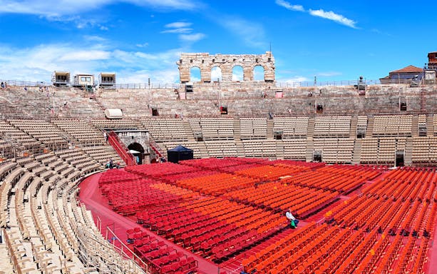Verona Arena seating area with red chairs under a blue sky.
