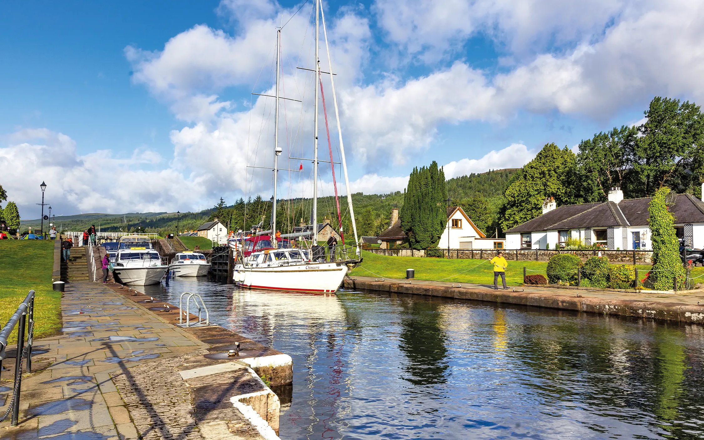 Boats docked along the canal in Fort Augustus, Scotland, with cottages and greenery nearby.