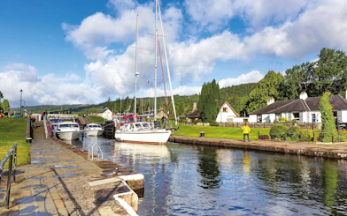Boats docked along the canal in Fort Augustus, Scotland, with cottages and greenery nearby.