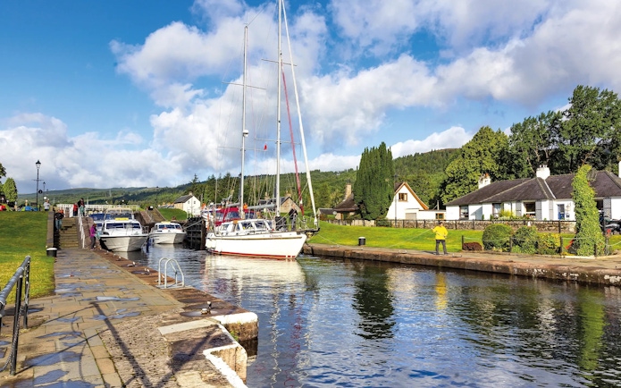 Boats docked along the canal in Fort Augustus, Scotland, with cottages and greenery nearby.