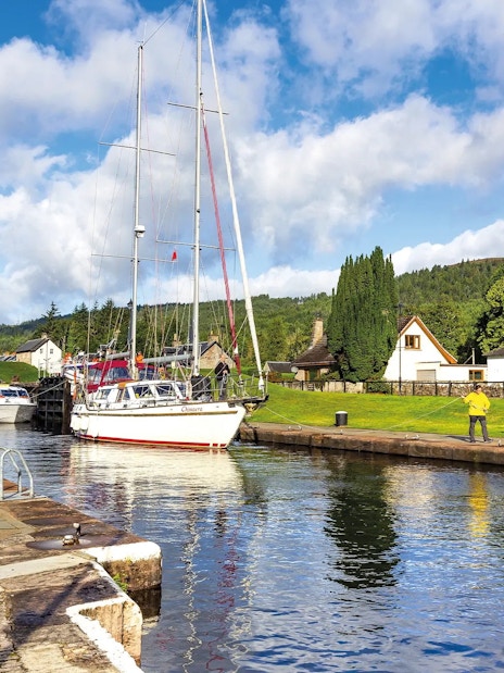 Boats docked along the canal in Fort Augustus, Scotland, with cottages and greenery nearby.