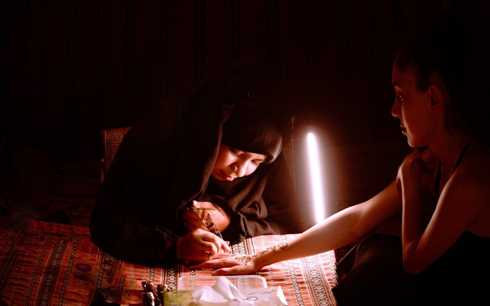 Henna artist applying design on woman's hand during desert safari overnight stay, Abu Dhabi.
