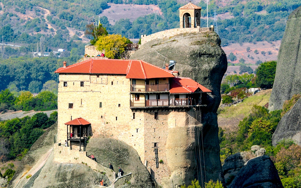 Meteora monastery perched on rock formation, surrounded by lush landscape, Greece.