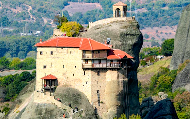 Meteora monastery perched on rock formation, surrounded by lush landscape, Greece.