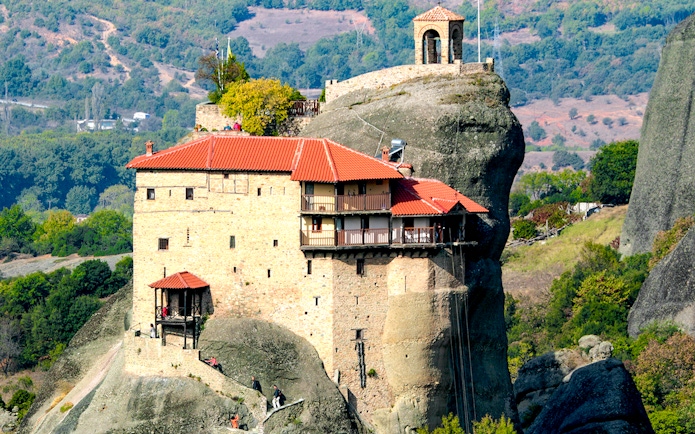Meteora monastery perched on rock formation, surrounded by lush landscape, Greece.