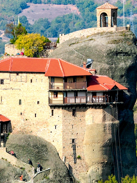 Meteora monastery perched on rock formation, surrounded by lush landscape, Greece.
