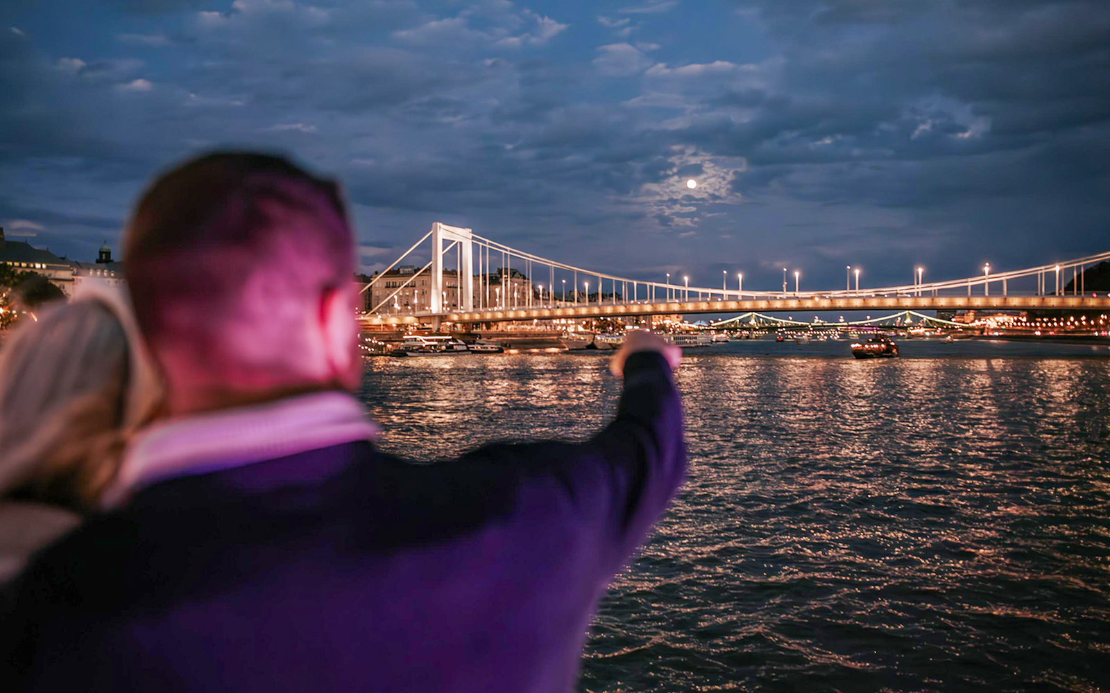 Guests pointing at illuminated bridge during Budapest Danube River Floating Beerfest.
