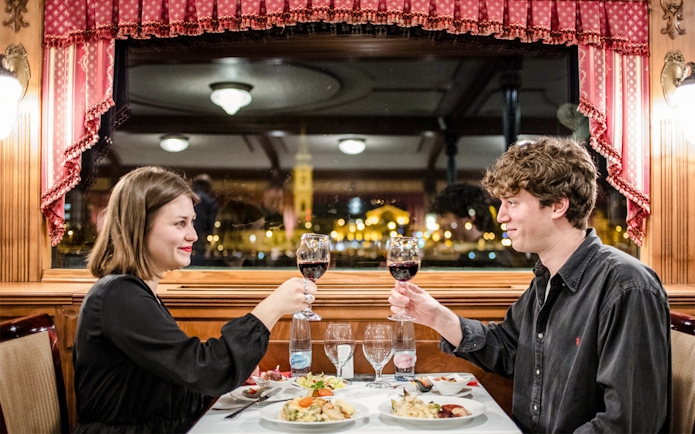 Couple toasting with wine on Danube dinner cruise at night.