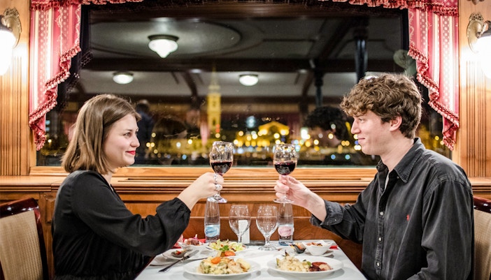 Couple enjoying wine on a Danube River sightseeing dinner cruise in Budapest at night.