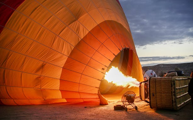 Hot air balloon inflating with flame at sunrise, preparing for flight.