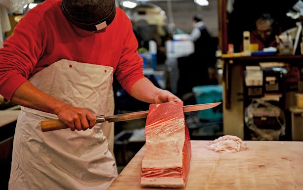 Chefs expertly filleting tuna at a bustling market.