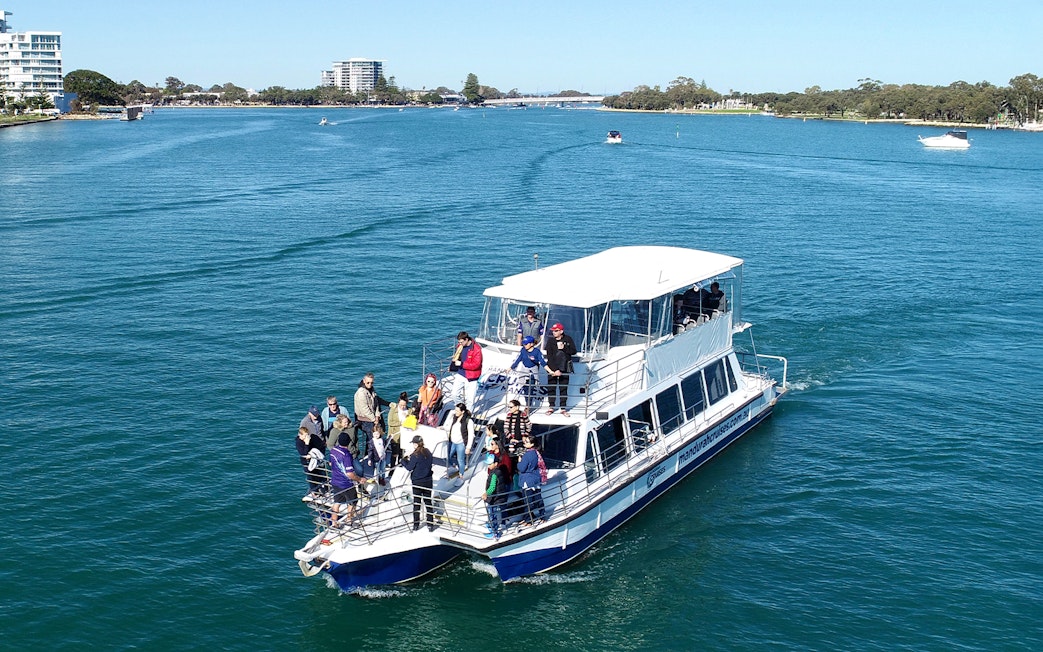 Tourists on a cruise boat in a scenic waterway with distant city skyline.