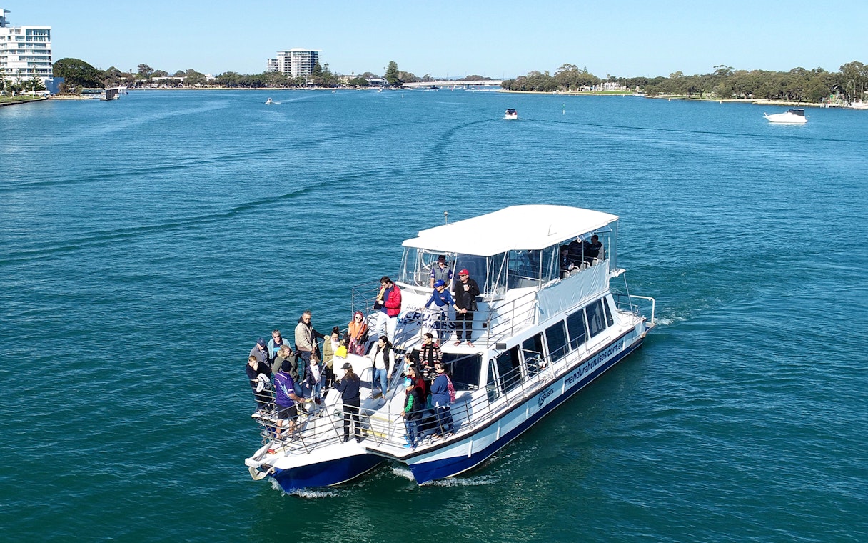 Tourists on a cruise boat in a scenic waterway with distant city skyline.