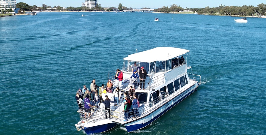 Tourists on a scenic marine cruise in Perth, Australia, watching dolphins in the ocean.