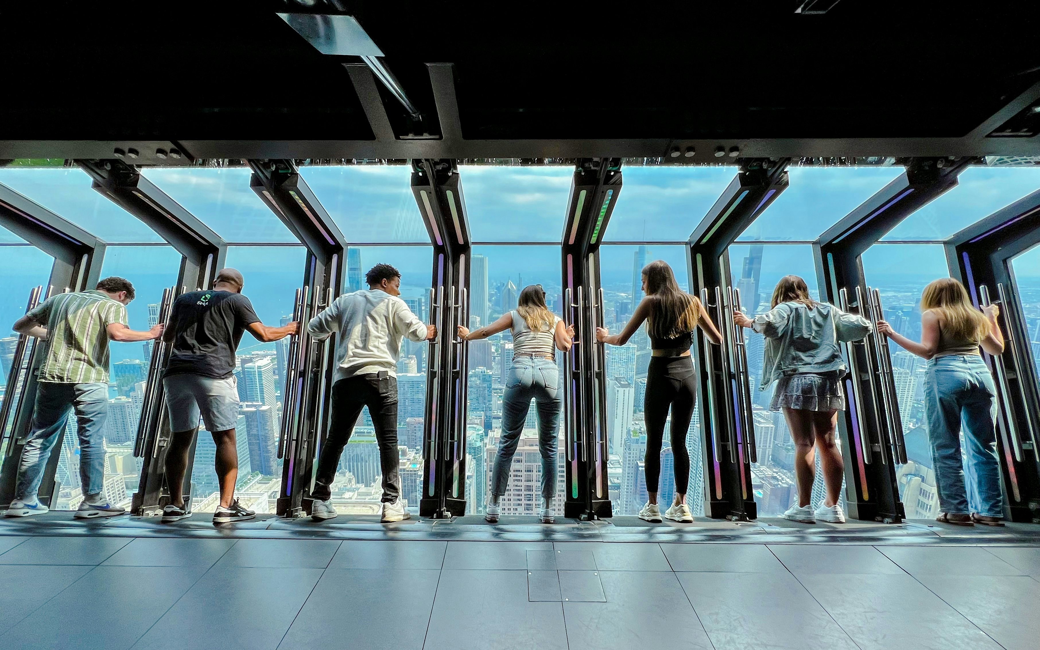 Visitors experiencing TILT at Chicago 360, leaning over the city skyline.