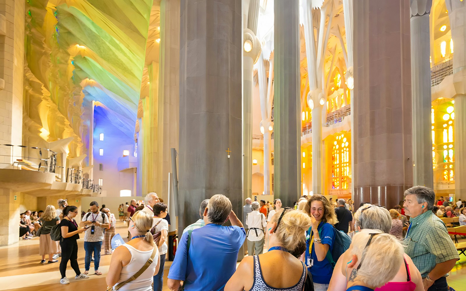 Tourists inside Sagrada Familia on a guided tour, Barcelona, with colorful stained glass windows.