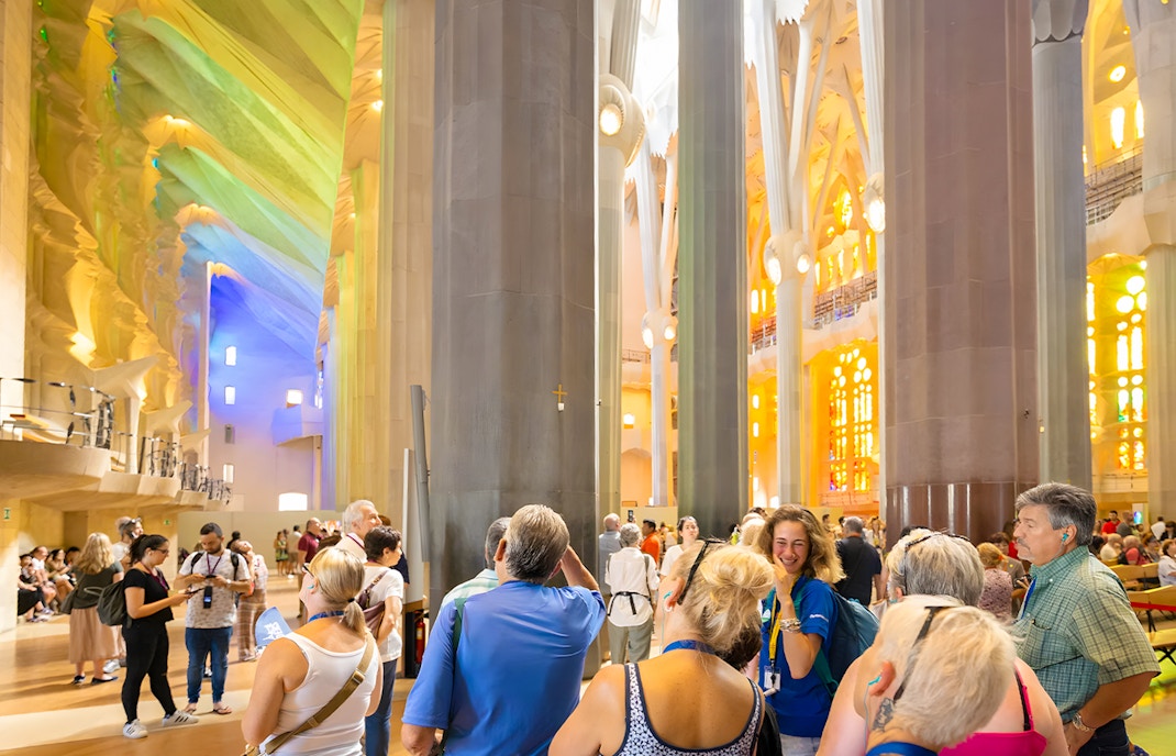 Tourists inside Sagrada Familia on a guided tour, Barcelona, with colorful stained glass windows.