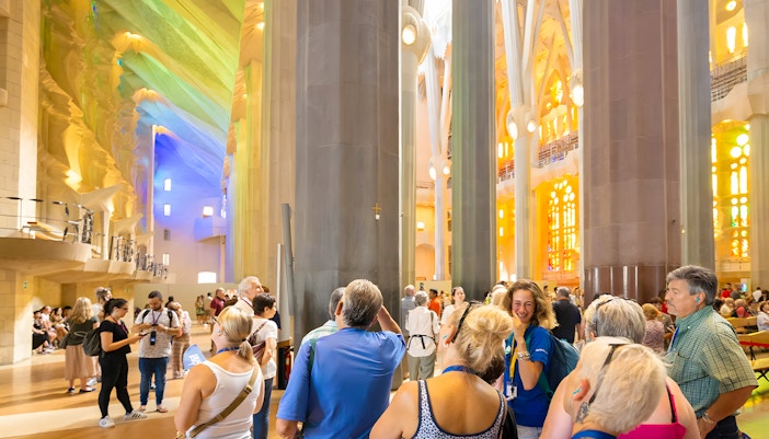 Tourists inside Sagrada Familia on a guided tour, Barcelona, with colorful stained glass windows.