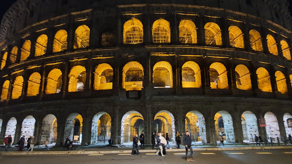 Roman Colosseum illuminated at night with few visitors in Rome, Italy.