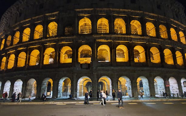 Roman Colosseum illuminated at night with few visitors in Rome, Italy.