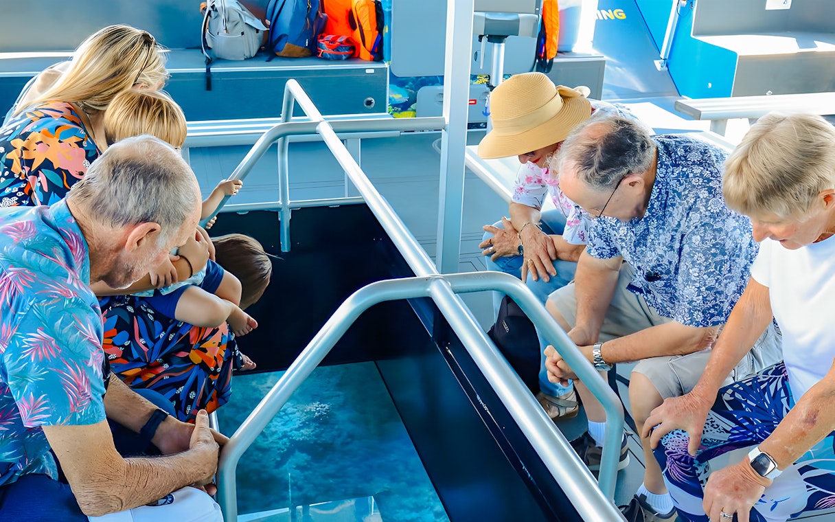 People observing marine life through glass floor on Airlie Beach Glass Bottom Boat tour.