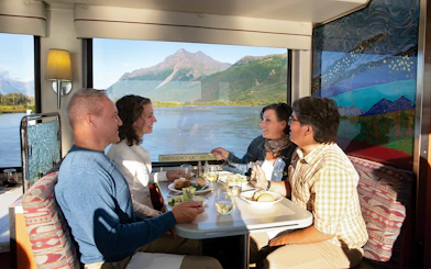 Passengers dining with mountain views on Alaska Railroad train.