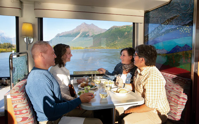 Passengers dining with mountain views on Alaska Railroad train.