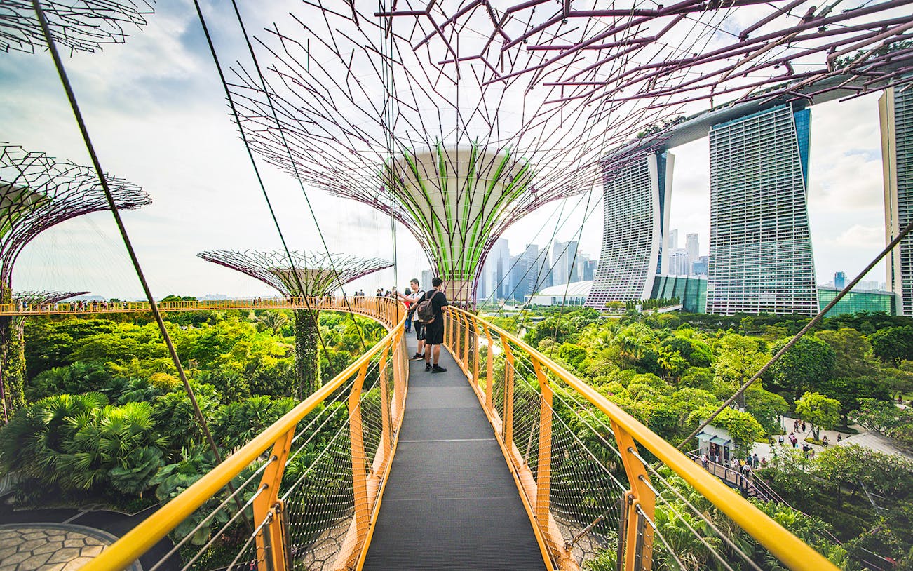 Visitors walking on OCBC Skywalk at Gardens by the Bay, Singapore, with city skyline in background.