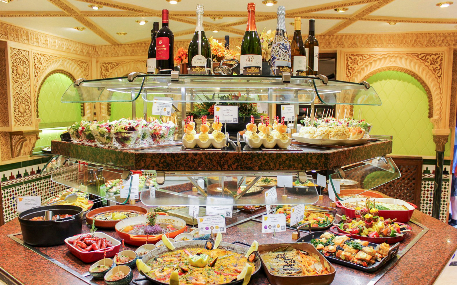 Food assortment at Tablao Cordobes buffet with paella, tapas, and wine bottles.