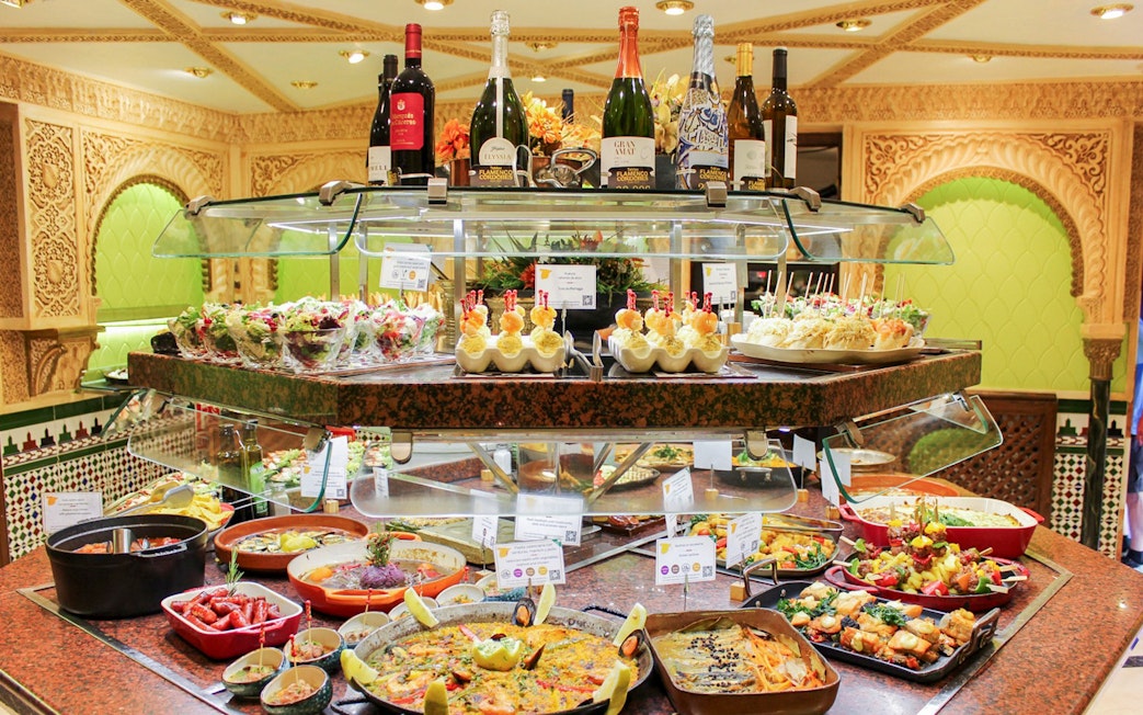 Food assortment at Tablao Cordobes buffet with paella, tapas, and wine bottles.