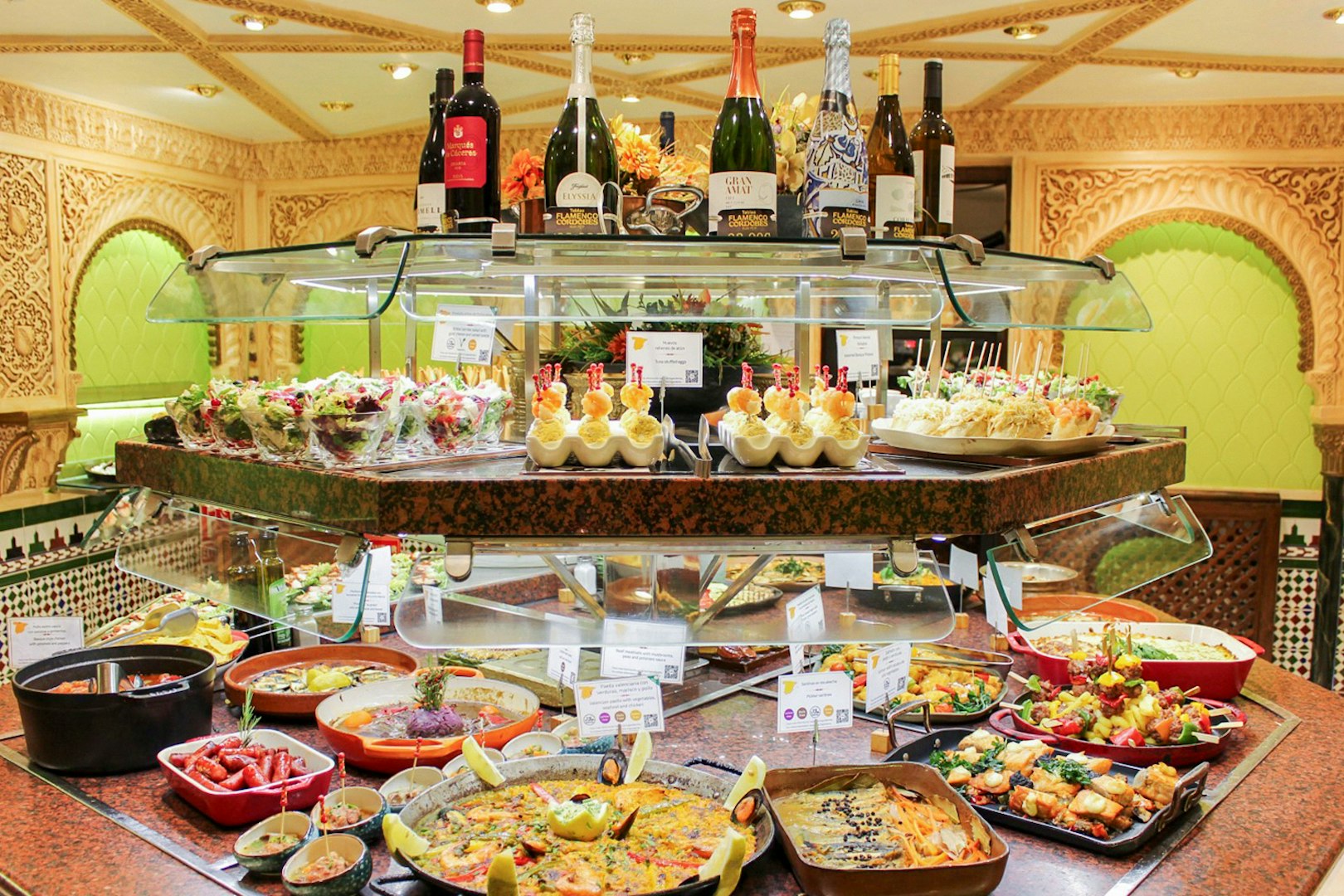Food assortment at Tablao Cordobes buffet with paella, tapas, and wine bottles.